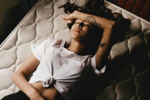 woman laying on mattress with arm on her forehead