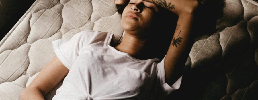 woman laying on mattress with arm on her forehead