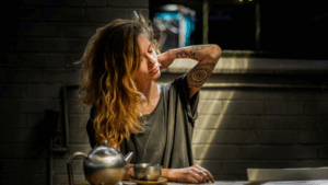 woman with tattoos making tea and looking stressed.