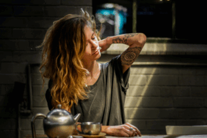 woman with tattoos making tea and looking stressed.