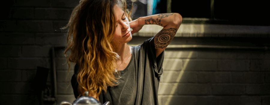 woman with tattoos making tea and looking stressed.