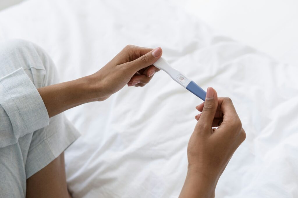 woman sitting on white bed holding positive pregnancy test