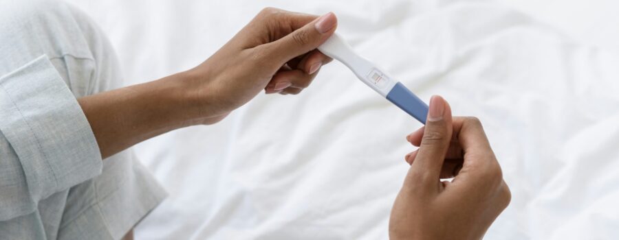 woman sitting on white bed holding positive pregnancy test