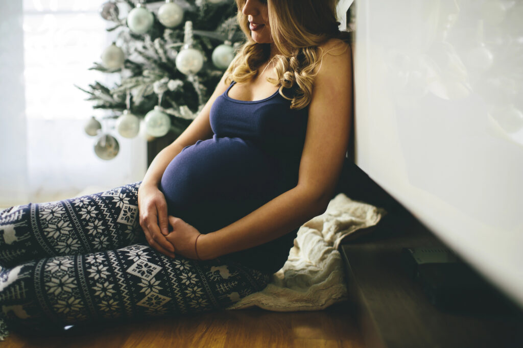 Pregnant woman sitting in front of a Christmas tree.