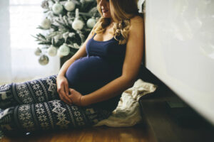 Pregnant woman sitting in front of a Christmas tree.