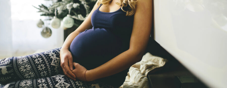 Pregnant woman sitting in front of a Christmas tree.